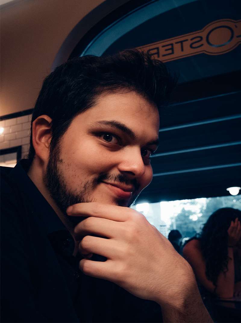Amadeus sitzt lächelnd in einem Restaurant und hat den Kopf auf die Hand gestützt.