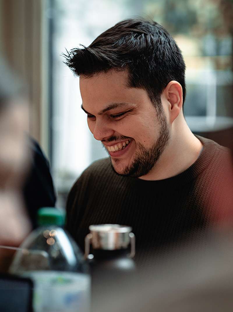 Amadeus sitzt lachend an seinem Arbeitsplatz im Coworking-Space.