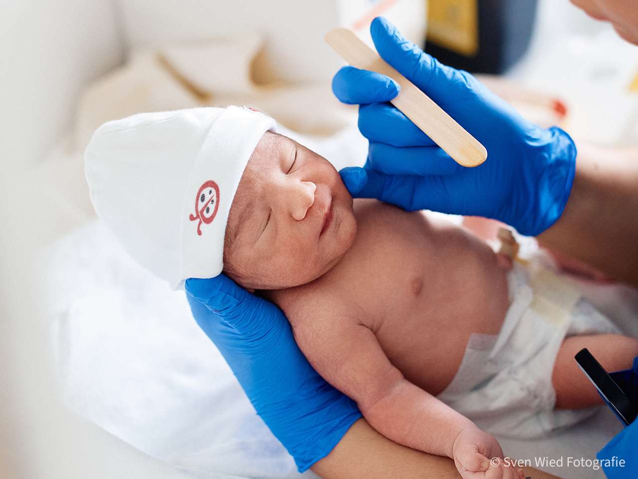 Ein Neugeborenes wird von einer Person mit blauen Handschuhen untersucht.
