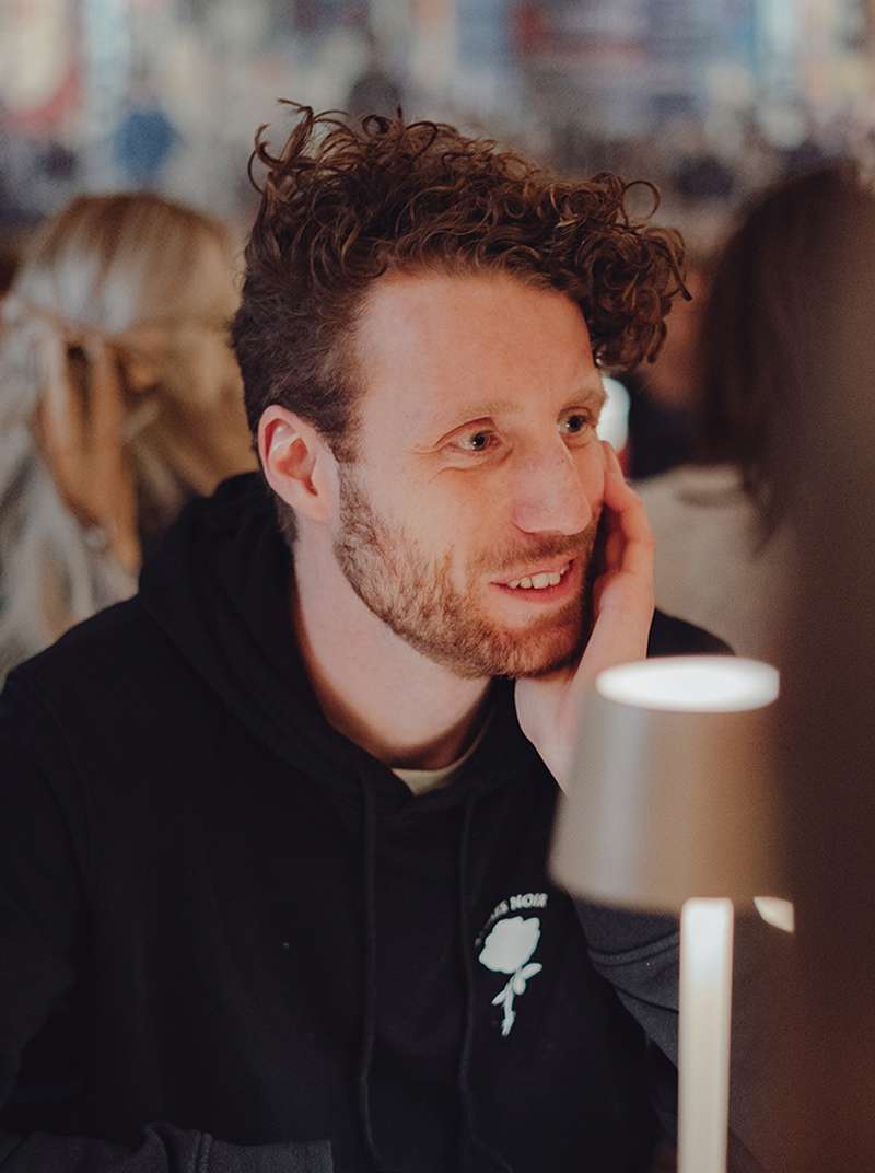 Michi hat das Kinn auf seine Hand gestützt und unterhält sich mit seinem Gegenüber